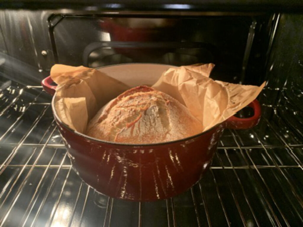 Pan ya horneado dentro de una olla de hierro fundido abierta, con la corteza formada y dorándose durante la fase final de cocción en horno doméstico.